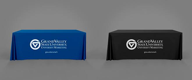 A table with a blue throw on it adjacent to a table with a black throw on it. Both throws have a white Grand Valley University Marketing logo on them.